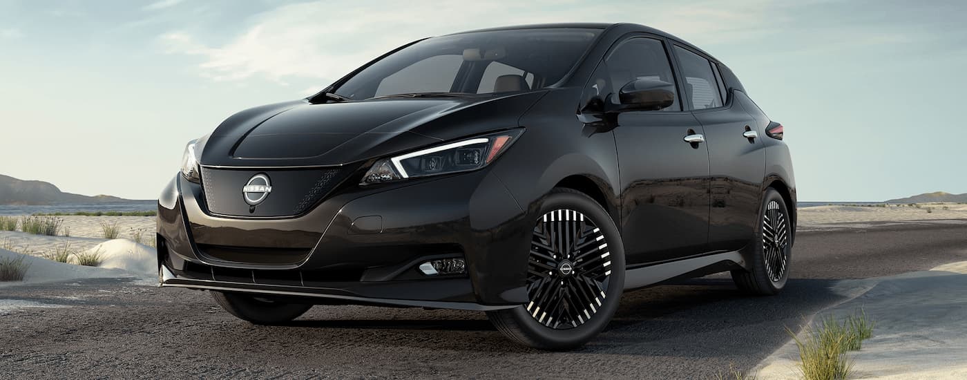 A black 2023 Nissan Leaf is shown driving on an open desert road.