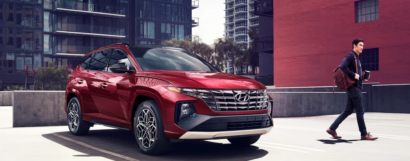 A man is shown walking away from a red 2024 Hyundai Tucson Hybrid N-Line parked on a lot.
