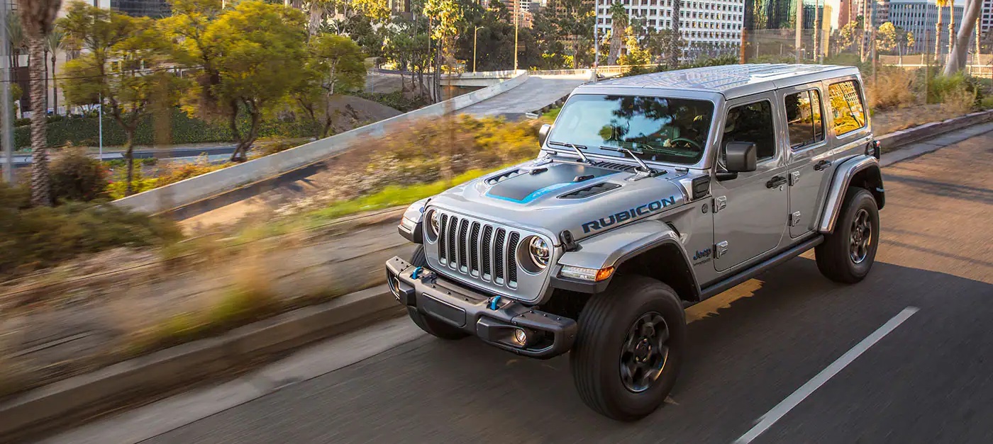 A silver 2022 Jeep Wrangler 4xe is shown driving on a city highway.