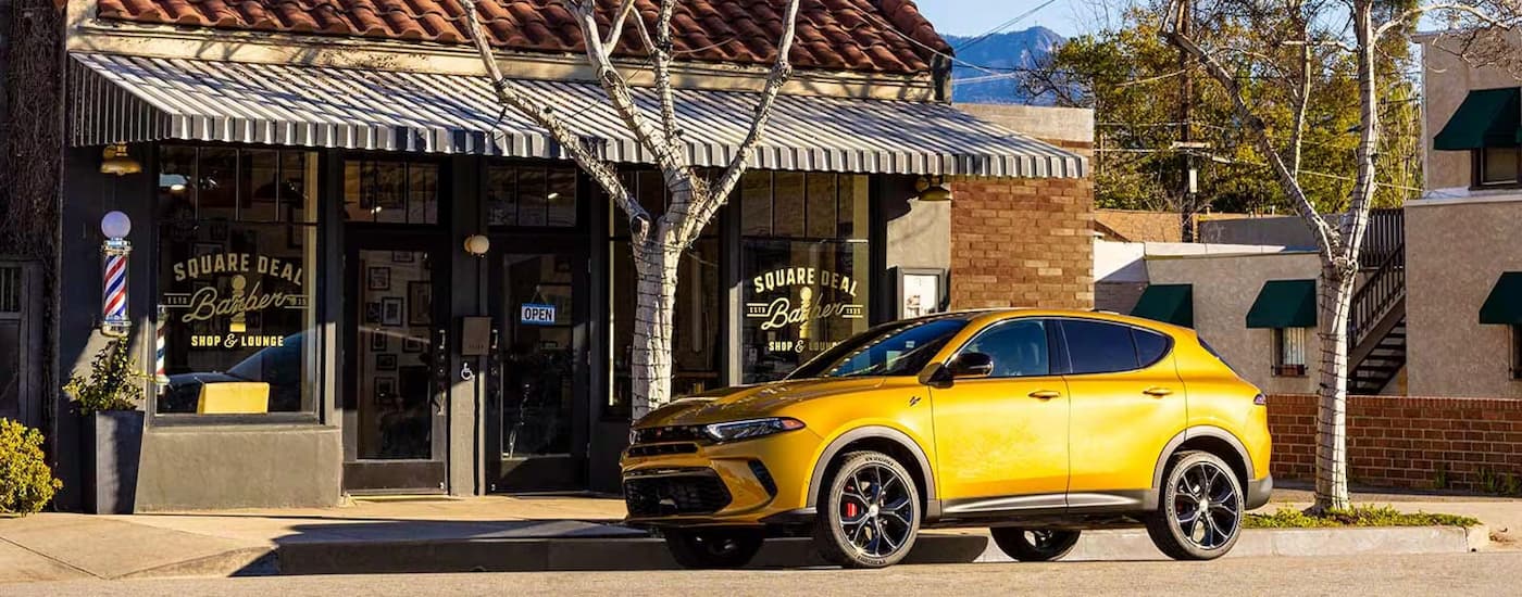 A gold 2024 Dodge Hornet R/T is shown parked on the side of a street in front of a barber shop.