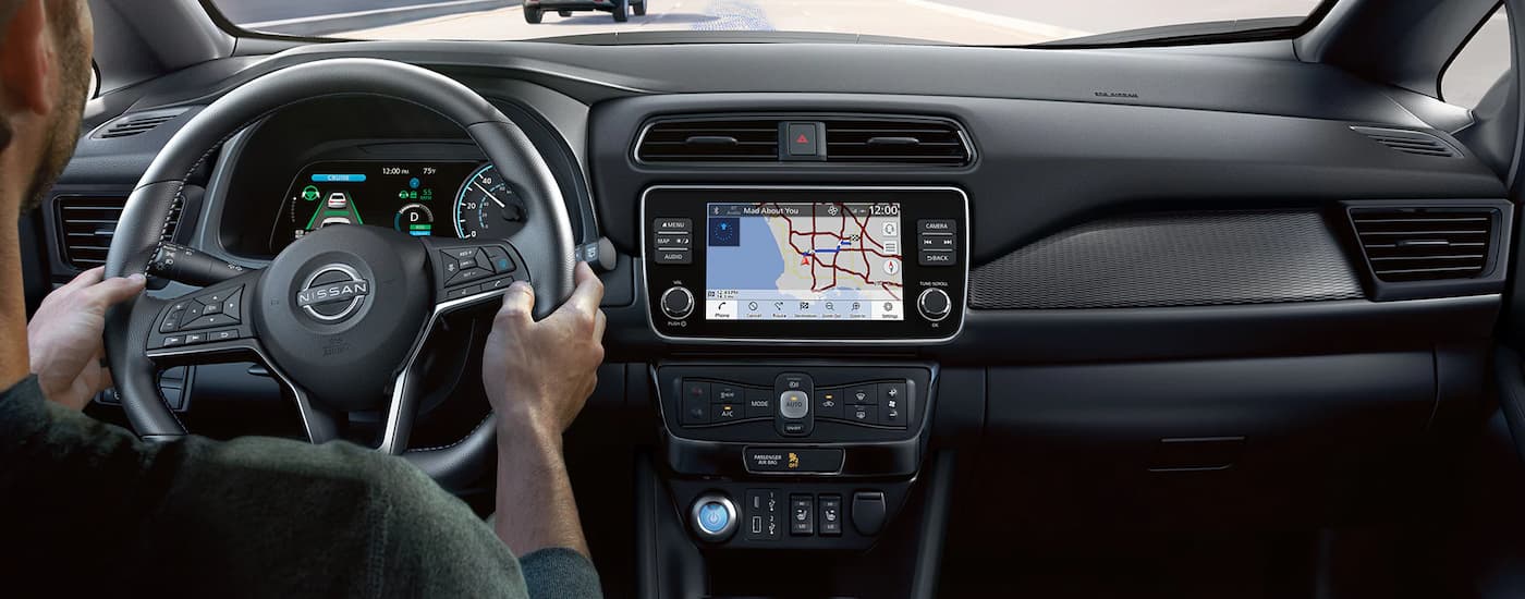 A man is shown driving a 2023 Nissan Leaf while using the map feature on the infotainment screen.