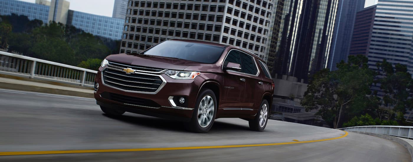 A maroon 2020 Chevy Traverse is shown driving on a highway away from a city.