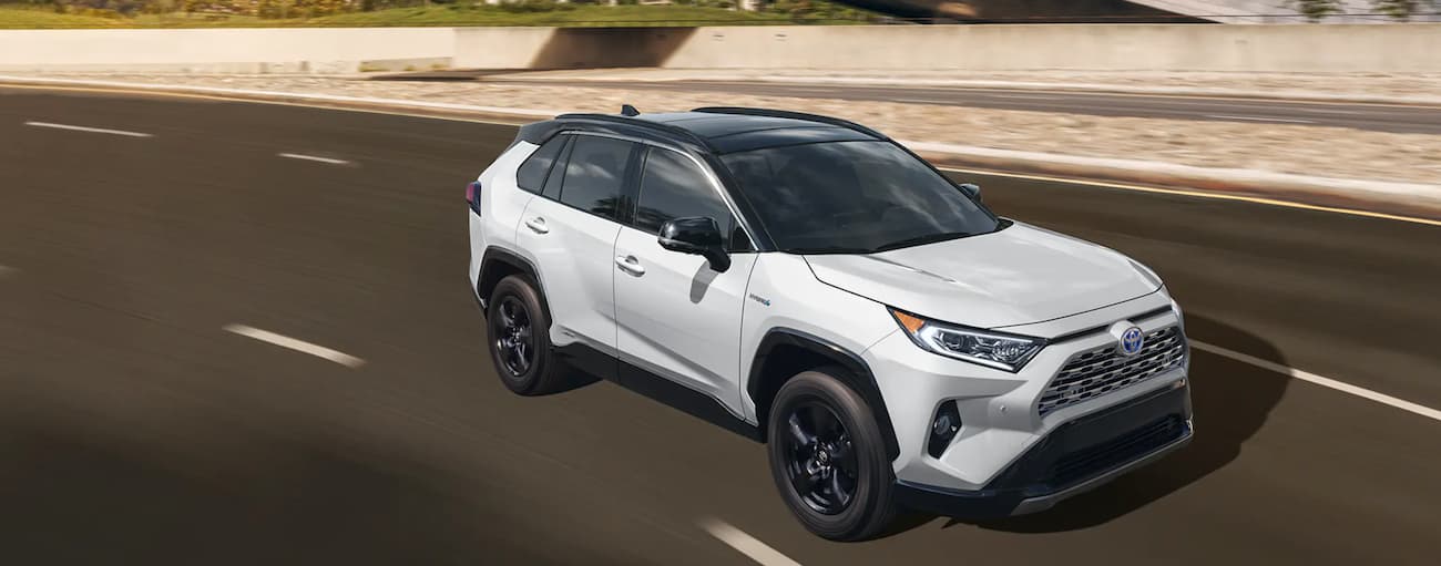 A white 2020 Toyota RAV4 is shown driving on an open freeway.