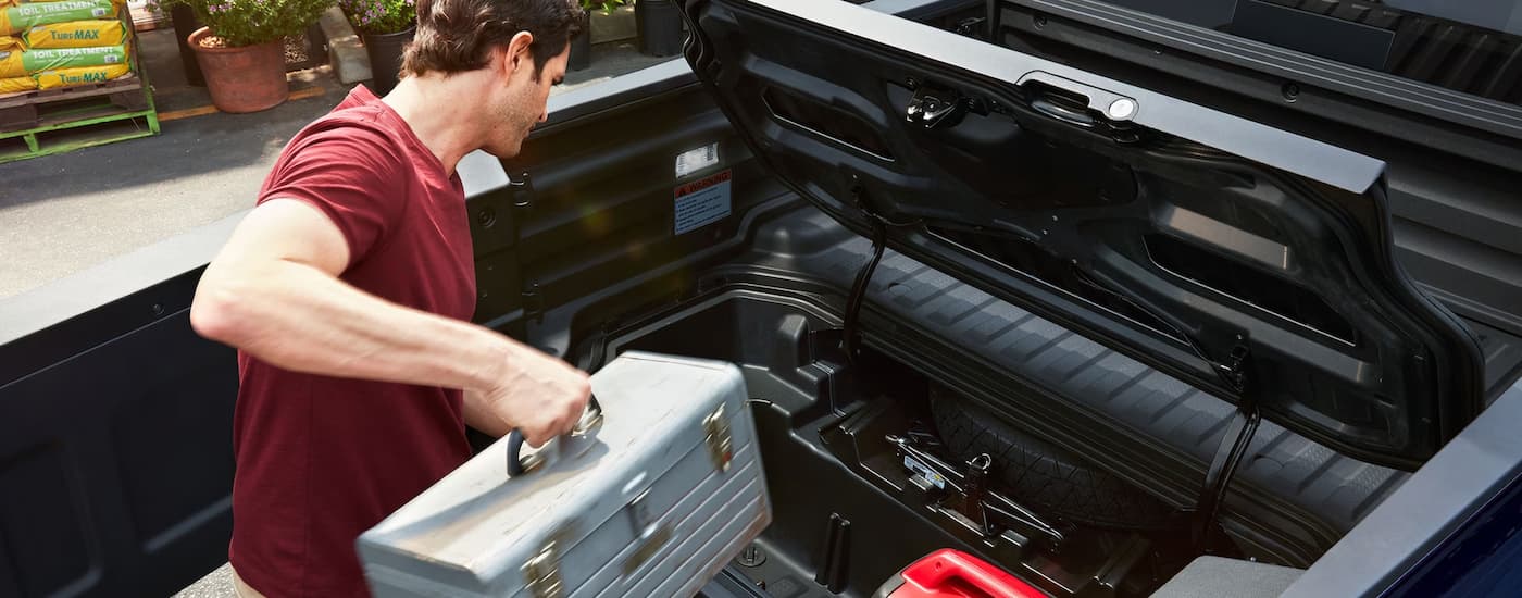 A man putting a toolbox in the lockable bed trunk of a silver 2023 Honda Ridgeline RTL-E.