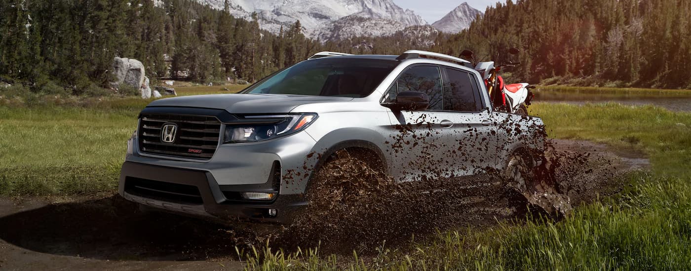 A silver 2023 Honda Ridgeline Sport splashes through mud while off-roading.