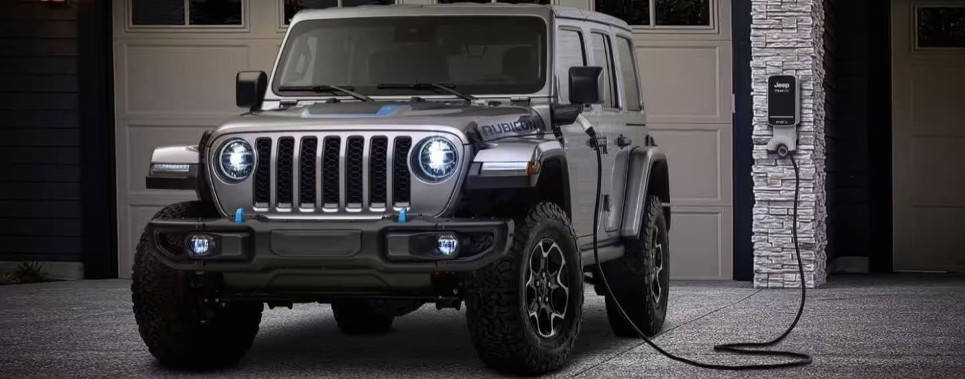 A grey 2024 Jeep Wrangler 4xe is shown charging on a driveway.