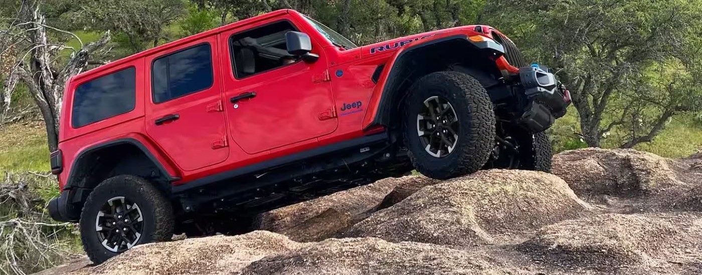 A red 2024 Jeep Wrangler 4xe is shown crawling over rocks after looking at electric vehicles for sale near St. Albert.