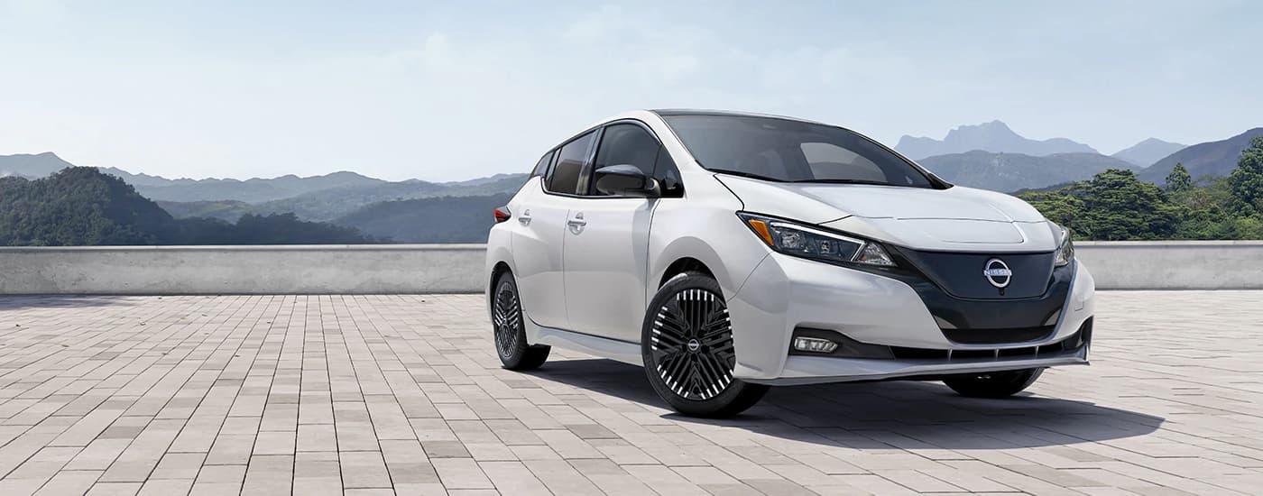 A white 2024 Nissan LEAF is shown parked on a stone area with a mountain view.