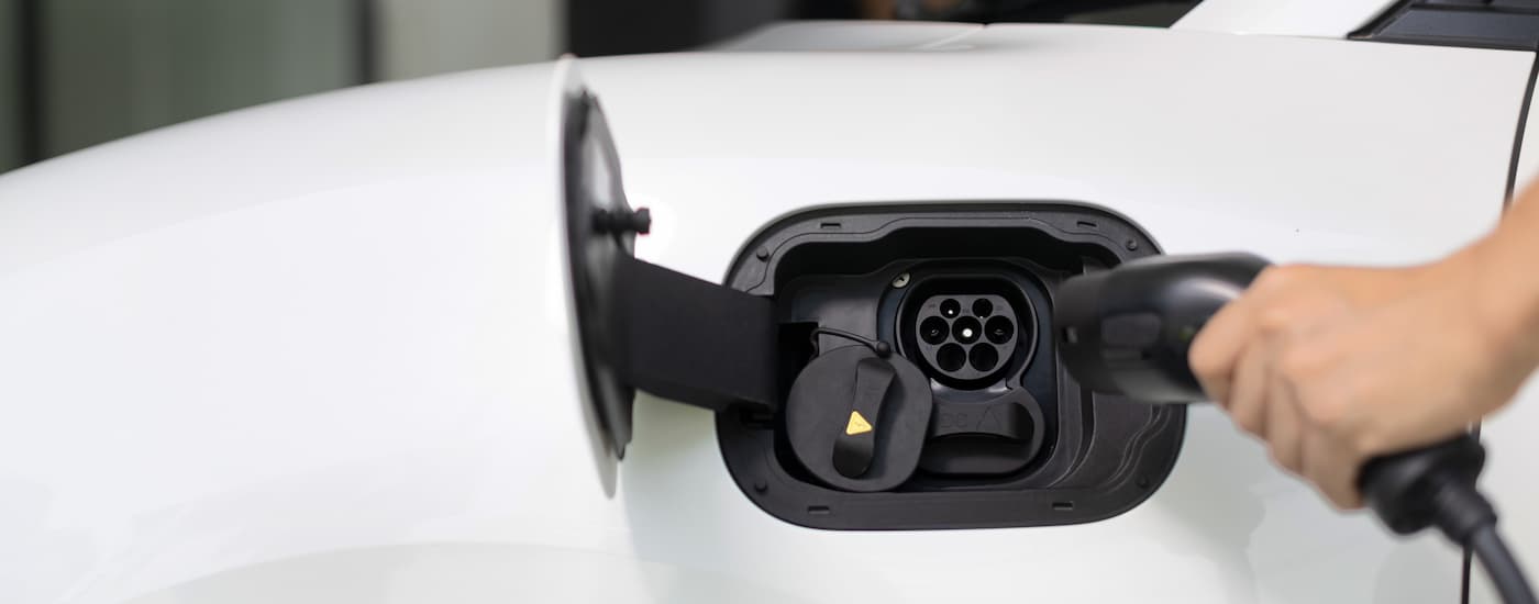 A close up of a person plugging an EV charger into a white vehicle.