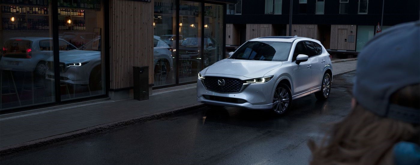 A white 2023 Mazda CX-5 for sale is shown parked on a city street.