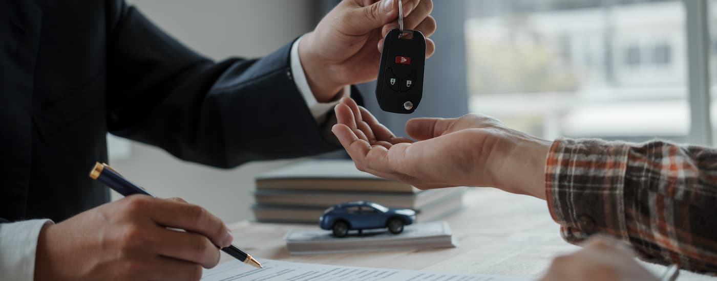 A salesman is shown handing a car key to a customer.
