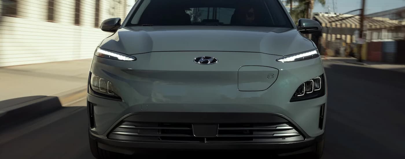 A grey 2023 Hyundai KONA Electric is shown from the front driving on a city street.