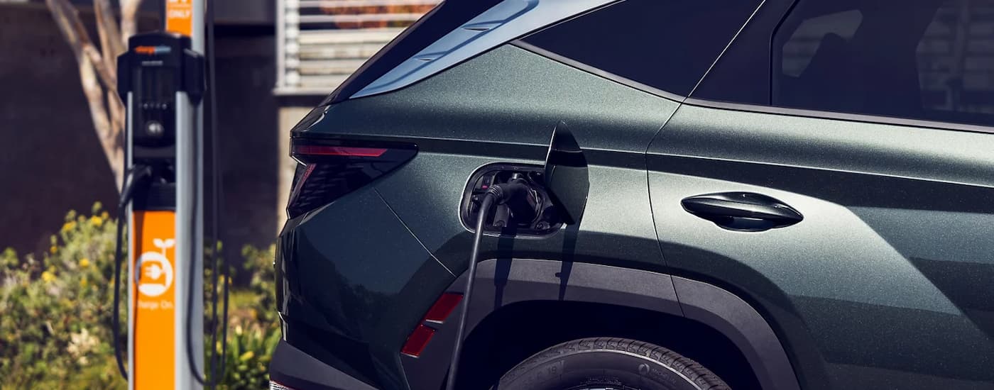 A grey 2023 Hyundai Tuscon PHEV is shown charging at an EV station.