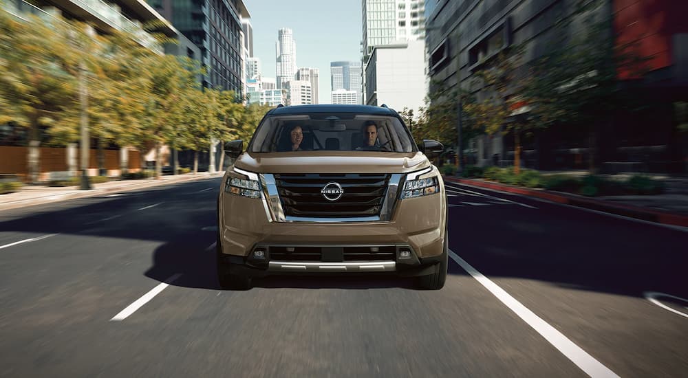 A brown 2023 Nissan Pathfinder is shown from the front driving on a city street to a Crystal Lake Nissan dealer.