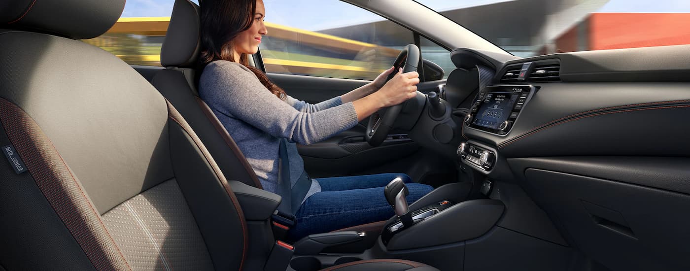 A woman is shown driving in a 2023 Nissan Versa SR on a busy city street.