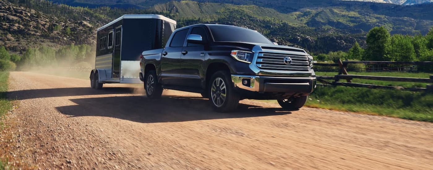 A black 2020 Toyota Tundra towing a black trailer on a dusty dirt road.