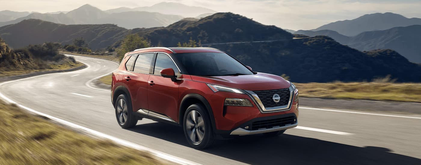 A red 2023 Nissan Rogue is shown driving on a mountain road after leaving a Crystal Lake Nissan dealer.