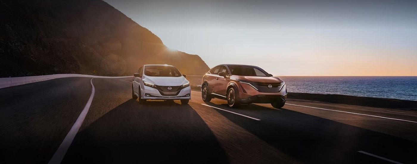 A white 2023 Nissan LEAF and a tan 2023 Nissan ARIYA are shown driving on a highway side by side.