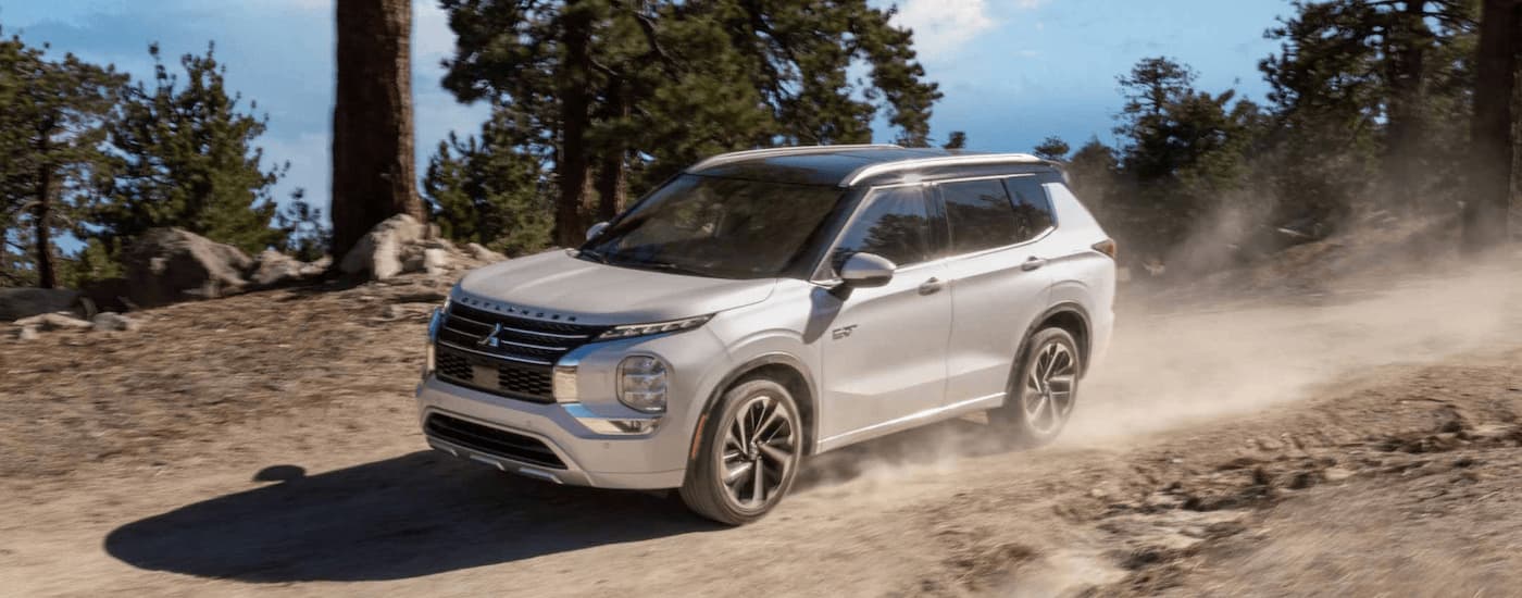 A white 2023 Mitsubishi Outlander PHEV is shown driving on a dusty dirt road while off-roading.