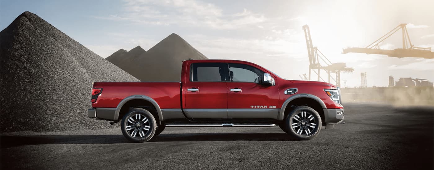 A red and grey 2024 Nissan Titan XD is shown from the side parked near a gravel pile.