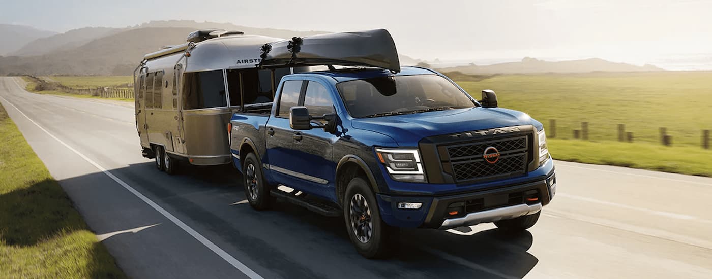 A blue 2024 Nissan Titan is shown towing a silver camper on an open highway.