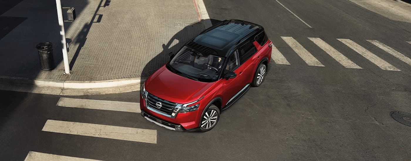 A red 2024 Nissan Pathfinder Platinum is shown driving on a city street during a test drive at a Crystal Lake Nissan dealer.