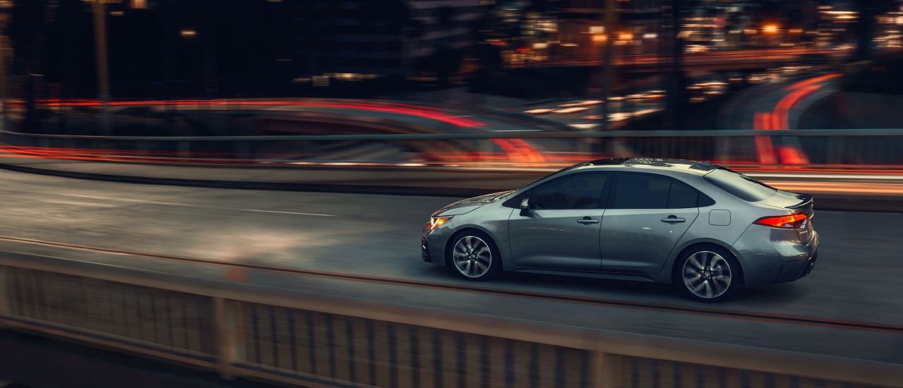 A silver 2021 Toyota Corolla is shown driving on a city bridge after leaving a used Toyota dealer.