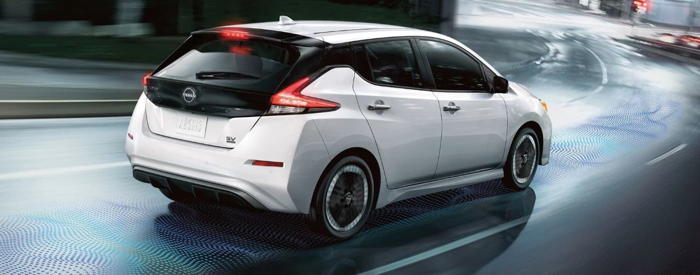 A white 2024 Nissan LEAF SV is shown driving on a wet city street.