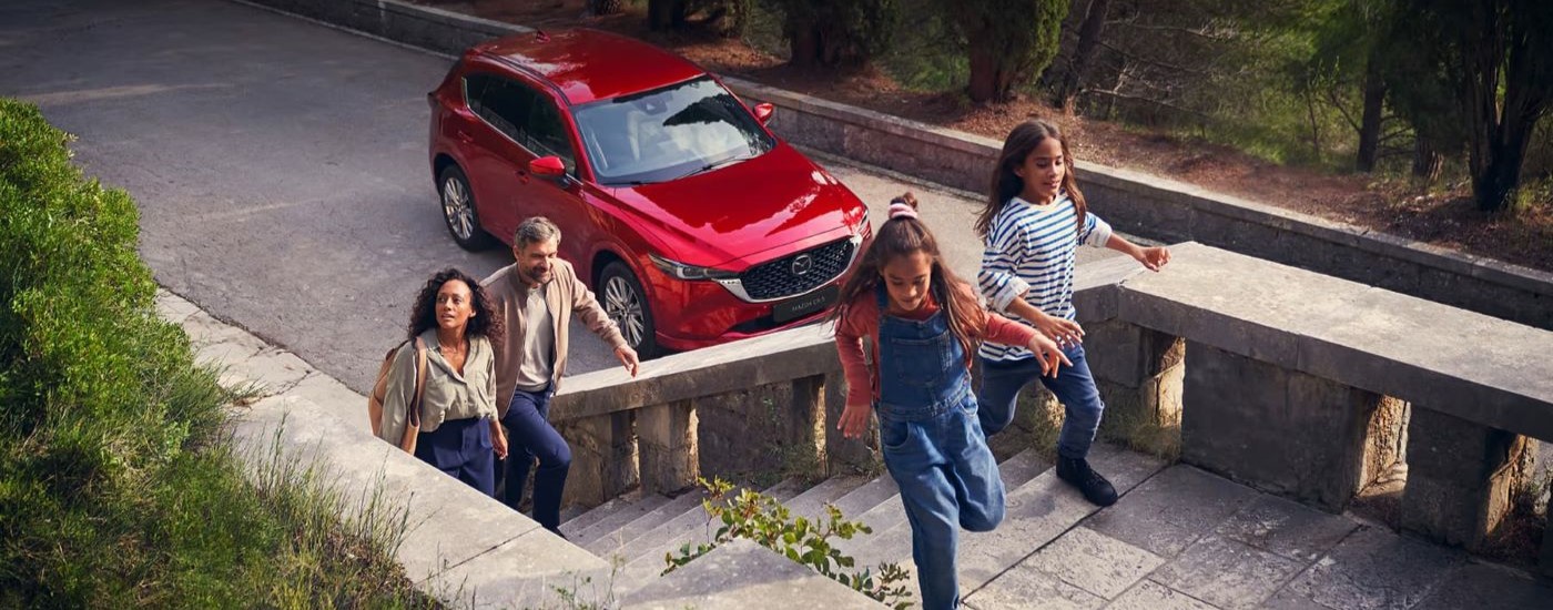A family is shown walking up stairs near a red 2023 Mazda CX-5.