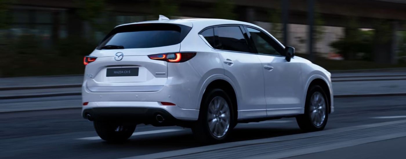 A white 2023 Mazda CX-5 is shown from the rear on a city street.