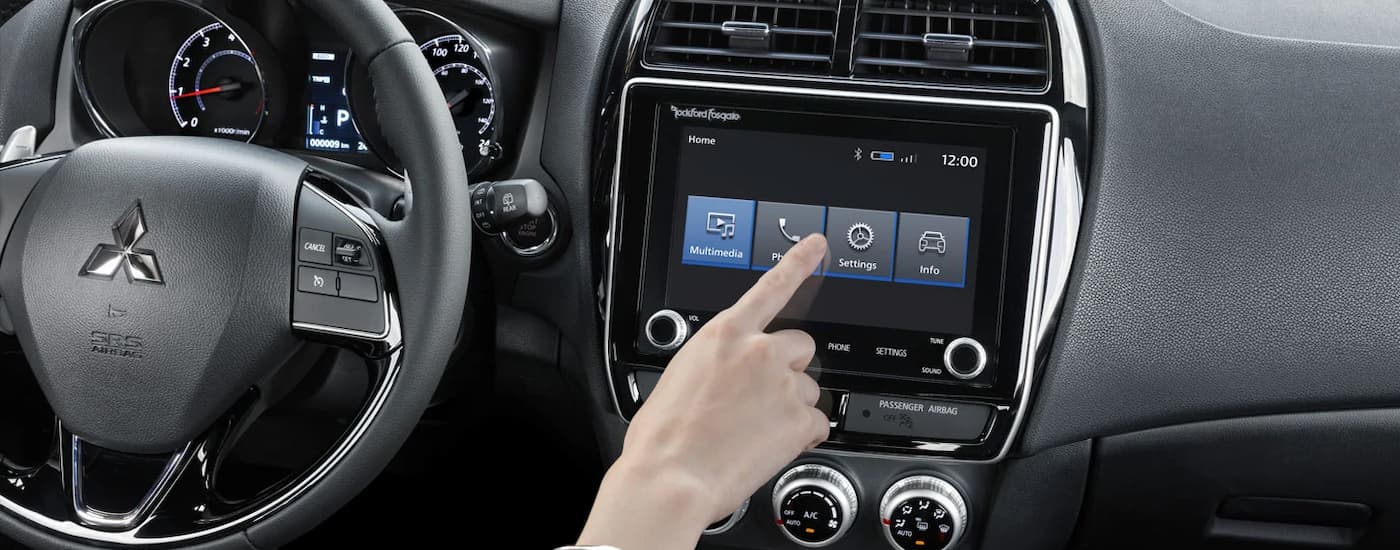 A person is shown using the infotainment screen in a 2024 Mitsubishi RVR.