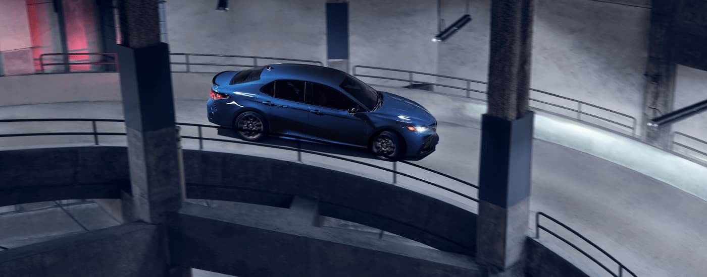 A blue 2024 Toyota Camry SE Nightshade is shown driving down a winding parking garage ramp.