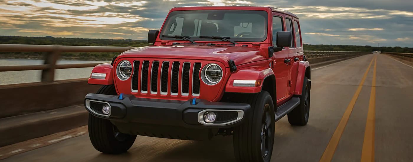 A red 2024 Jeep Wrangler is shown driving on a long brudge after viewing Jeep SUVs.