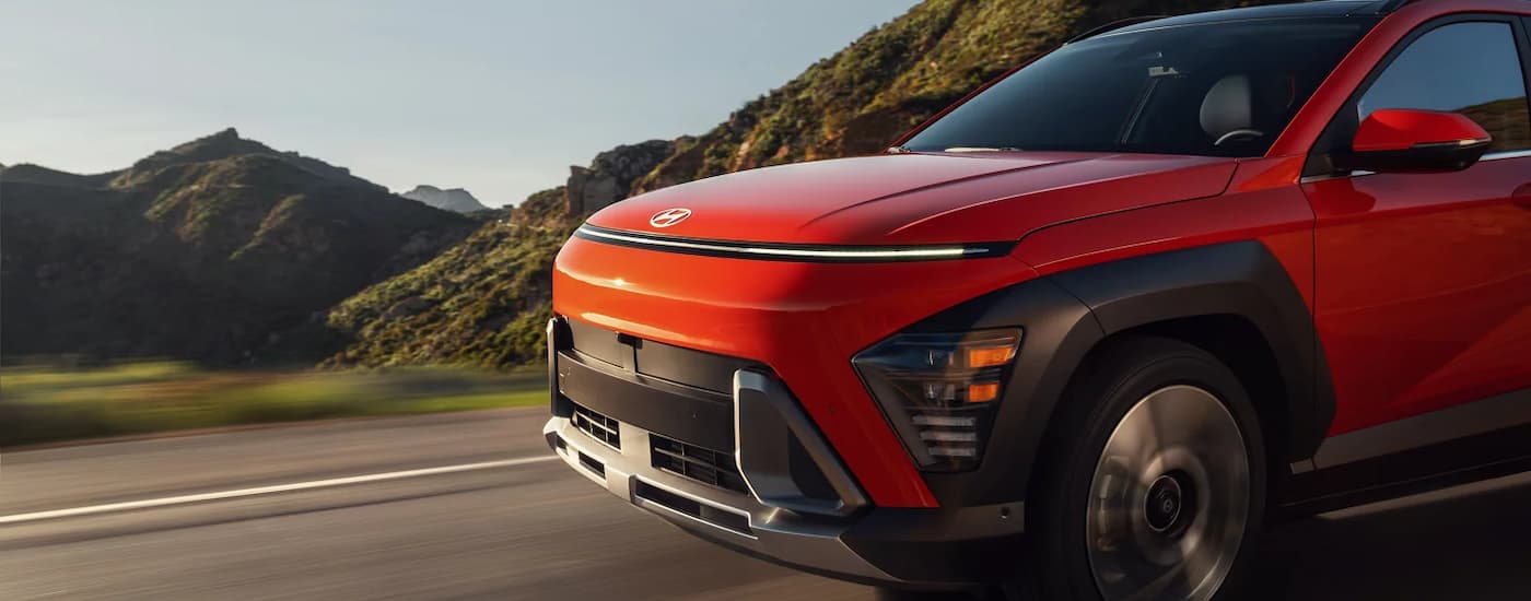  A popular Hyundai Kona for sale, an orange 2024 Hyundai Kona Limited, is shown driving on an open road.