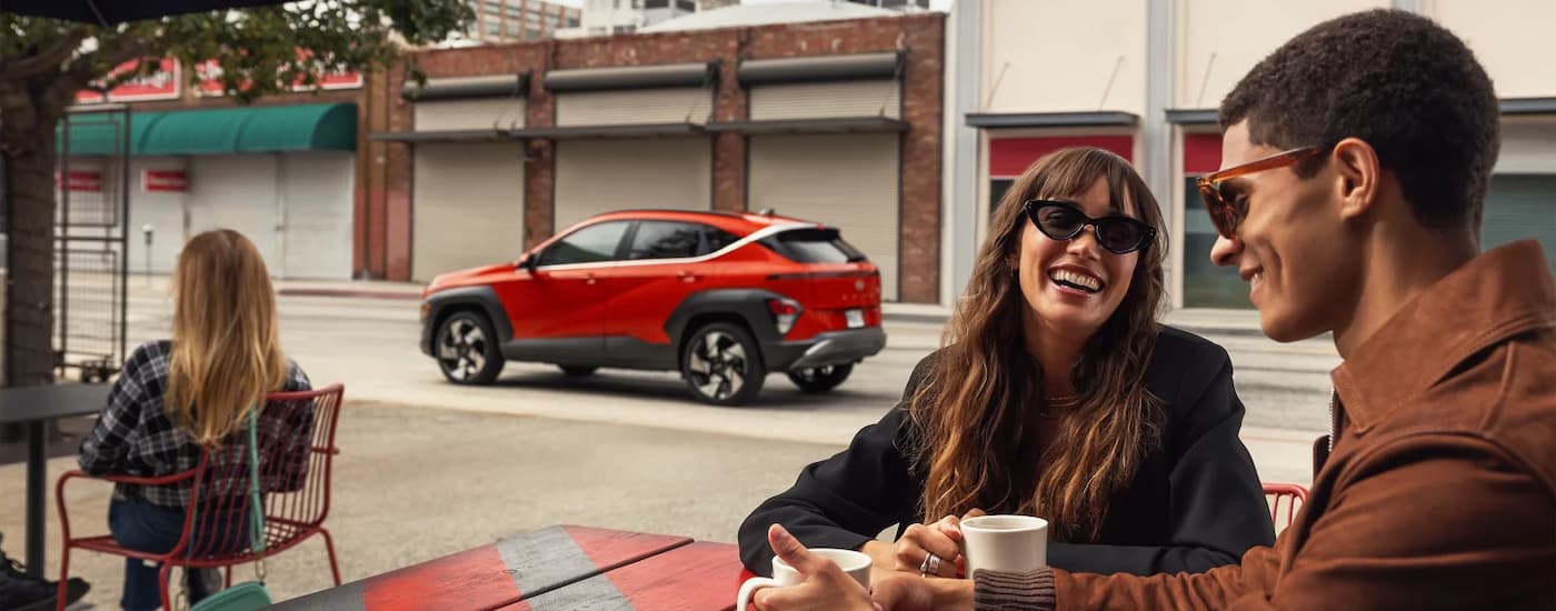 An orange 2024 Hyundai Kona Limited is shown from the side driving past a cafe.
