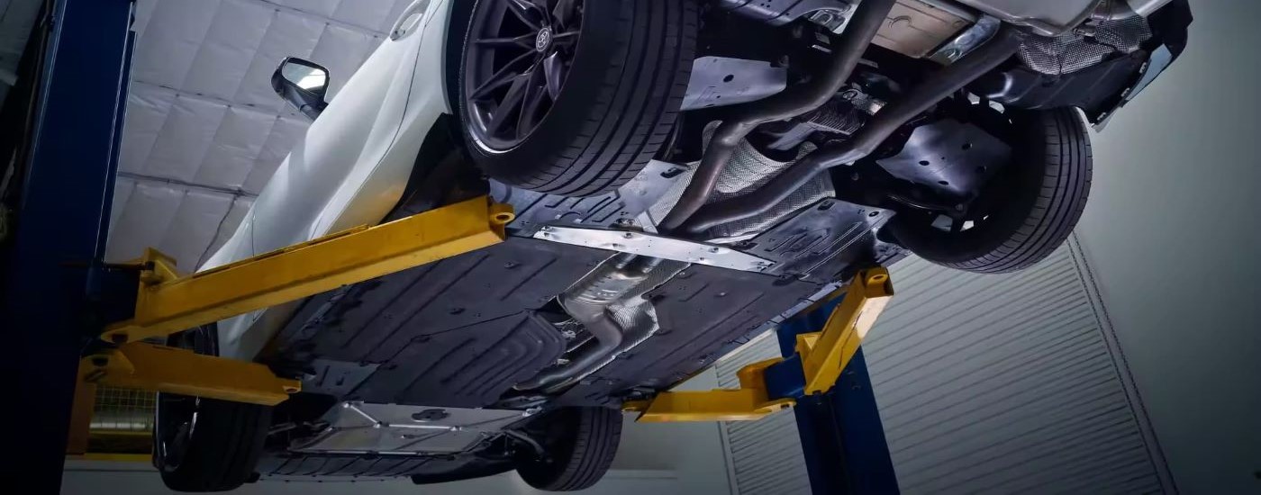 The undercarriage of white 2023 Toyota GR Supra is shown on a lift.