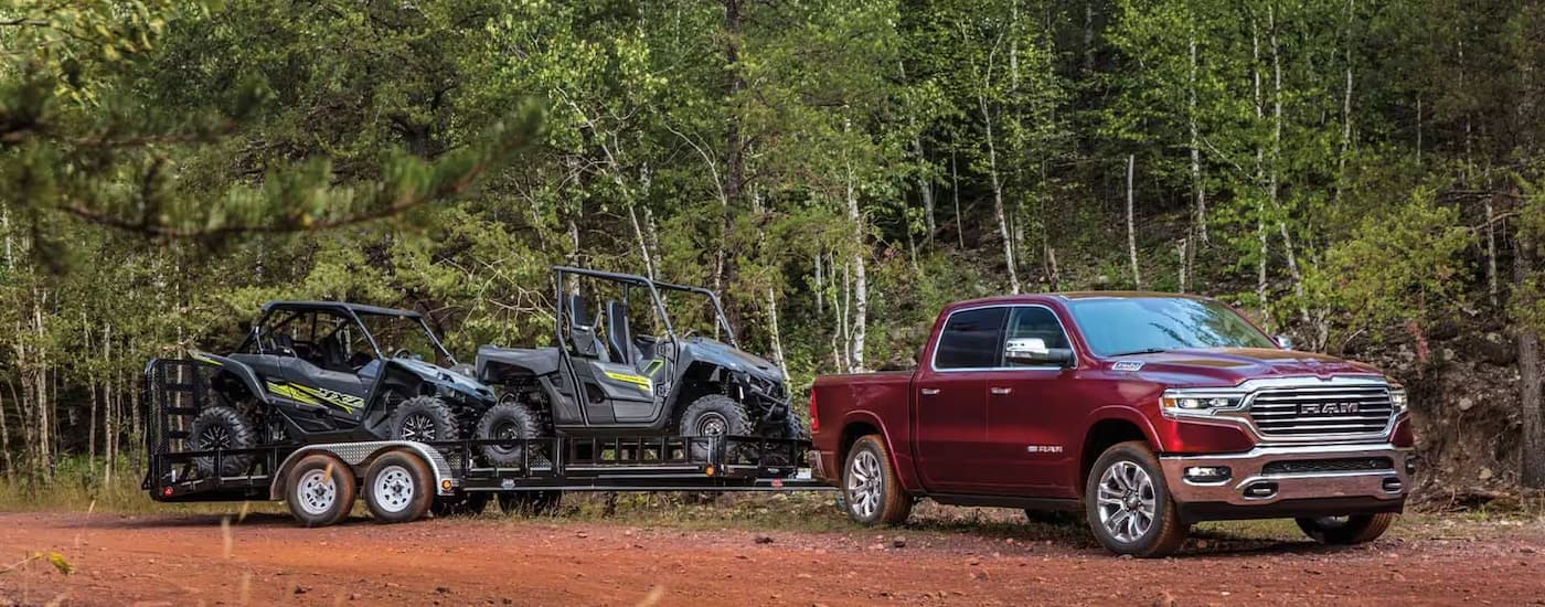 A red 2023 Ram 1500 is shown towing UTVs on a trailer after leaving a Ram dealer near Spruce Grove.