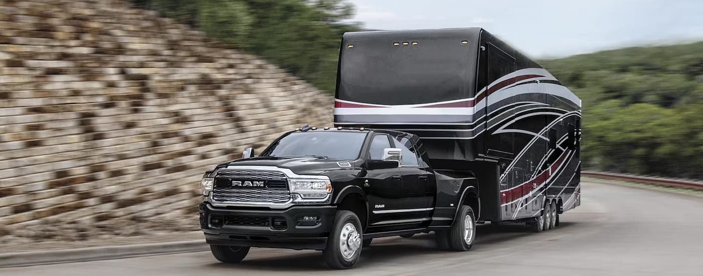 A black 2023 Ram 3500 is shown towing a large camper on a winding road.