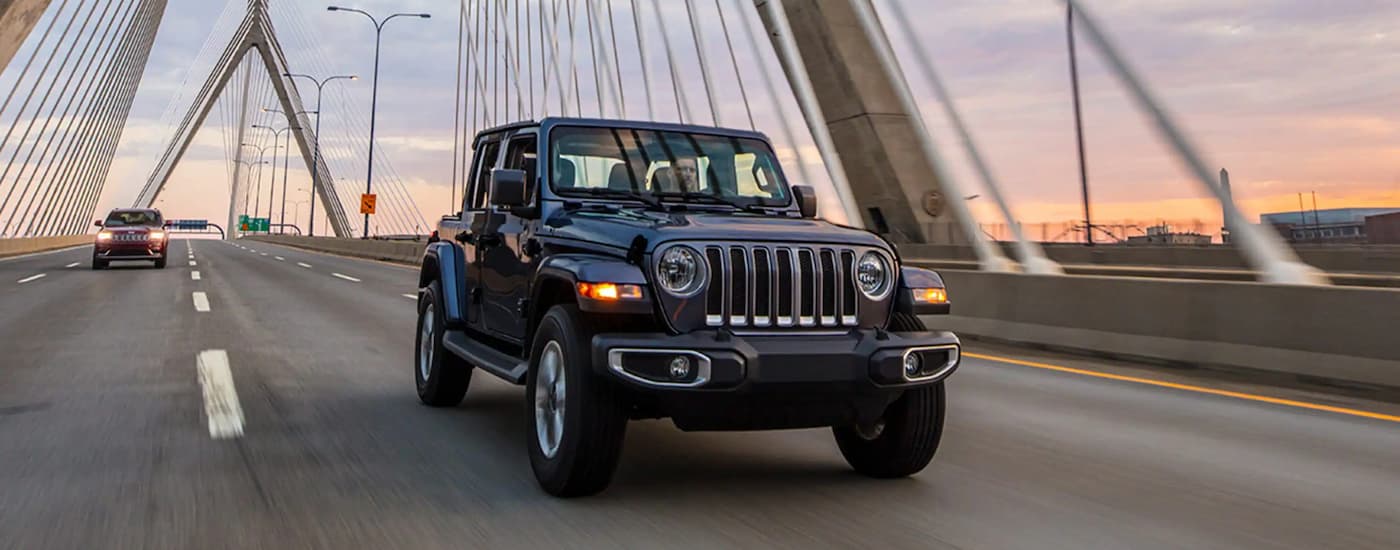 A black 2023 Jeep Wrangler is shown driving on a bridge after leaving a Jeep dealer near Spruce Grove.