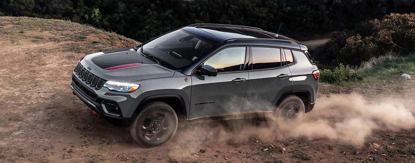 A grey 2023 Jeep Compass Trailhawk is shown driving on a dusty dirt road.