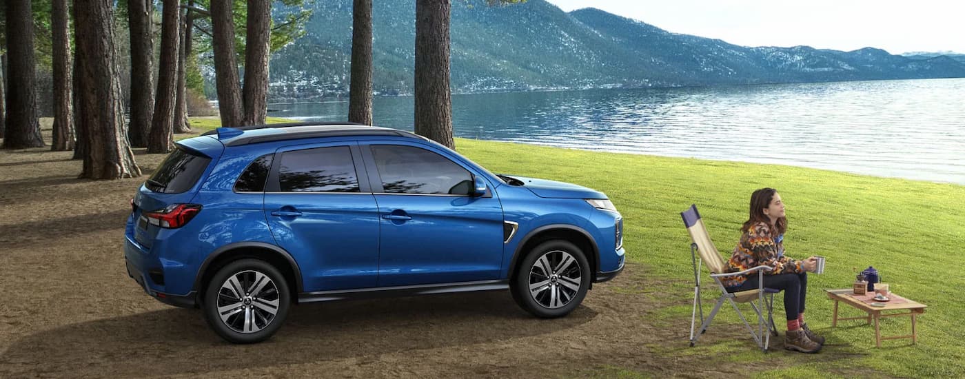 A blue 2024 Mitsubishi RVR is shown from the side parked at a campsite near a lake.