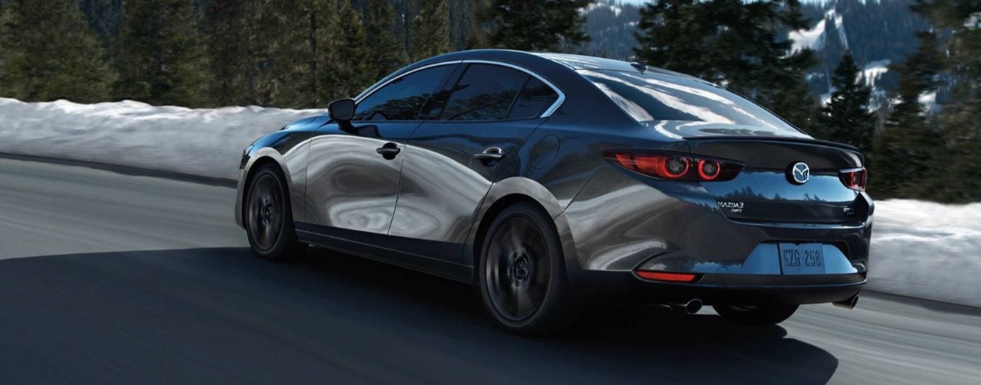 A grey 2024 Mazda3 is shown from the side driving on a snowy road.