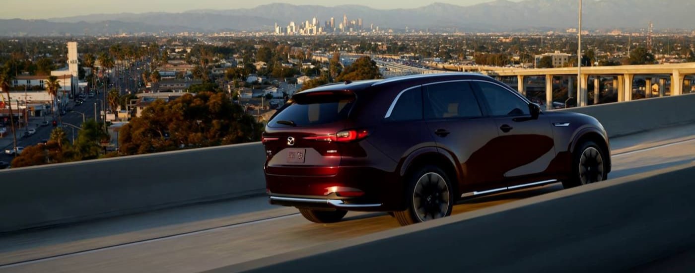 A maroon 2024 Mazda CX-90 is shown driving on an overpass.