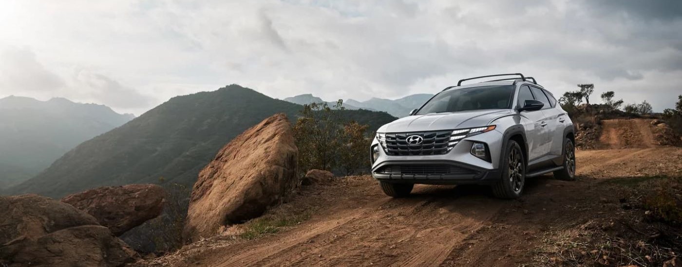 A silver used 2023 Hyundai Tucson XRT for sale is shown off-roading on a dirt road.