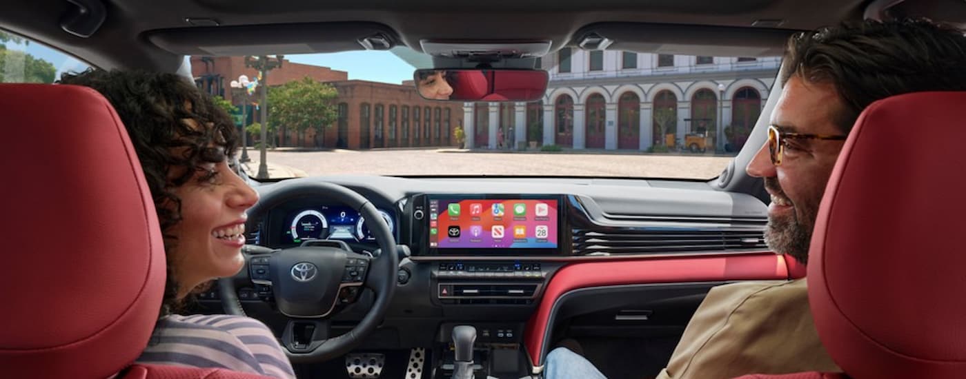 A woman and a man are shown in the red front seats of a 2025 Toyota Camry.