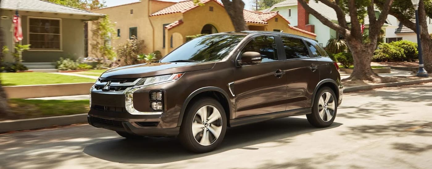 A brown 2024 Mitsubishi RVR for sale is shown driving through a neighborhood.