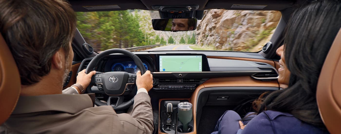 A man and a woman are shown driving a 2025 Toyota Crown Signia on mountainside road.
