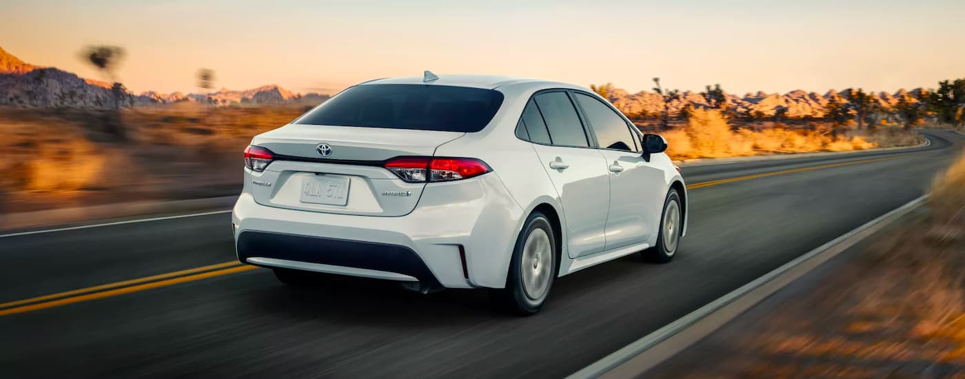 A white 2021 Toyota Corolla Hybrid LE is shown driving on an open road.