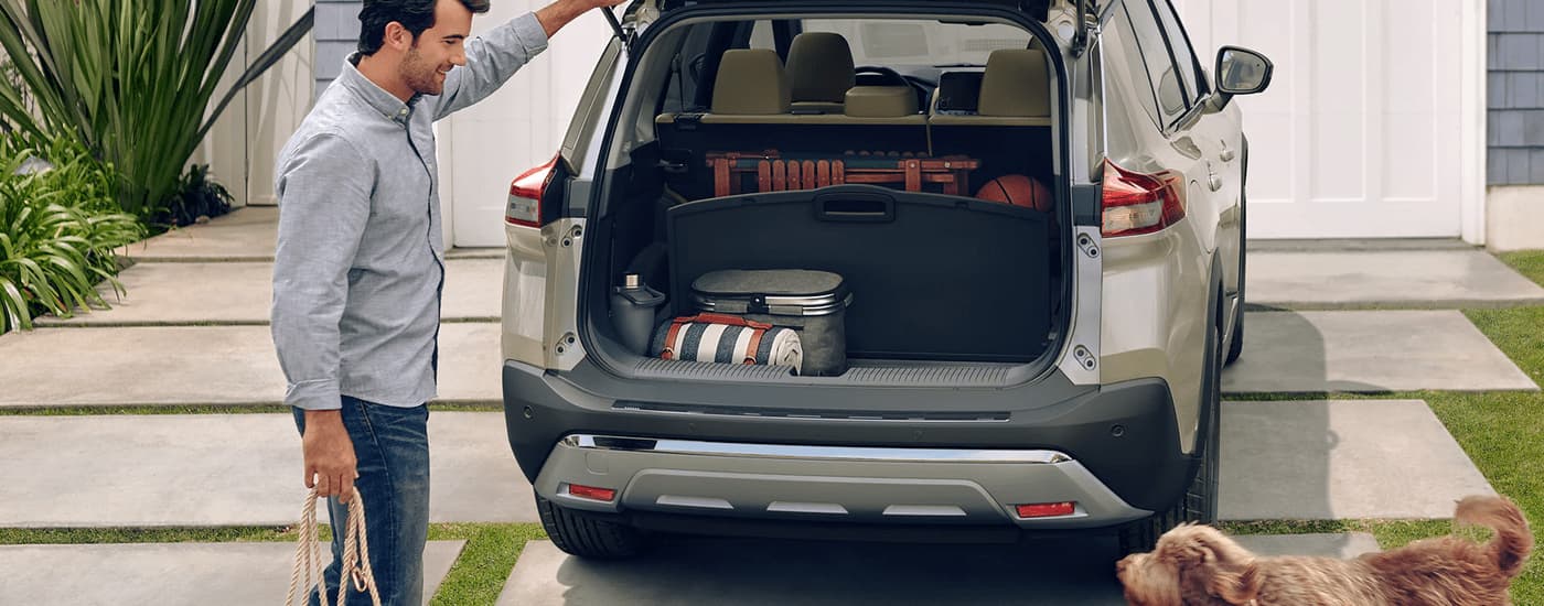 A man is shown putting cargo in the back of a 2022 Nissan Rogue in a driveway.