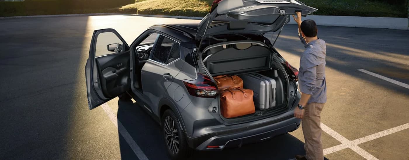 A man is shown loading suitcases in to the rear of a grey 2024 Nissan Kicks.